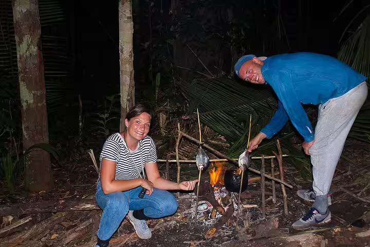 Campers cooking fish over an open fire during an Amazon Survival Tour at night.