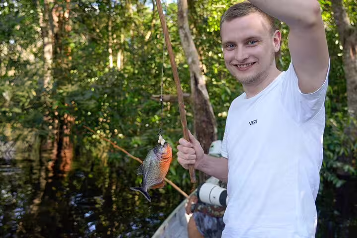 Man proudly holding a freshly caught piranha in the Amazon rainforest during a survival tour adventure.
