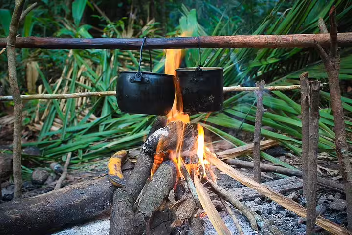 Campfire cooking with pots over open flames in lush Amazon rainforest at Tapiri Floating Lodge for immersive jungle experience.