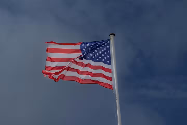 American flag waving on a white flagpole against a stormy dark blue sky