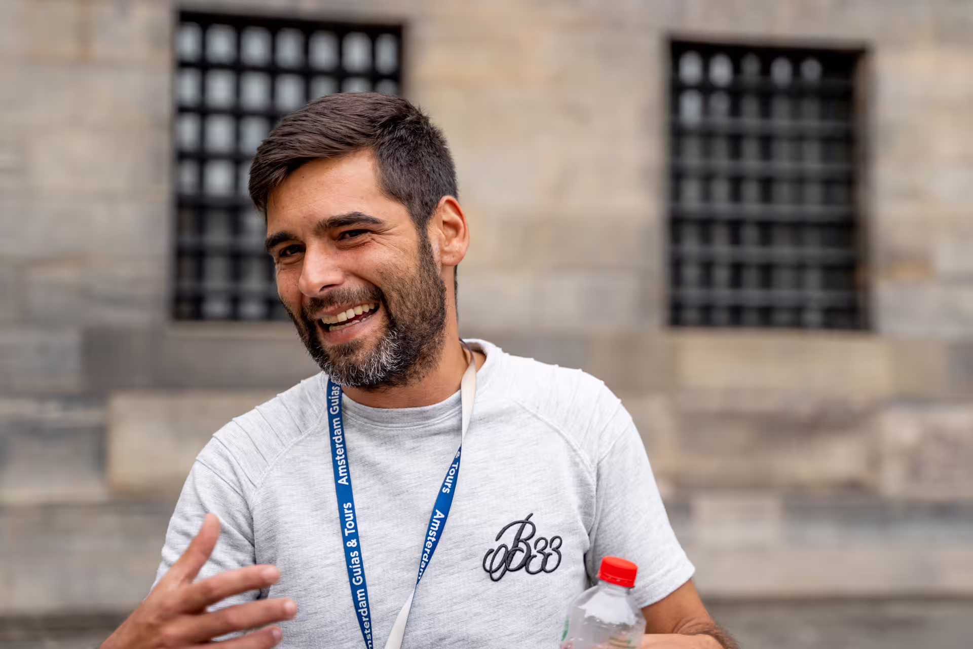 A smiling tour guide with a lanyard and water bottle leads an engaging Amersfoort walking tour, departing from Amsterdam by train.