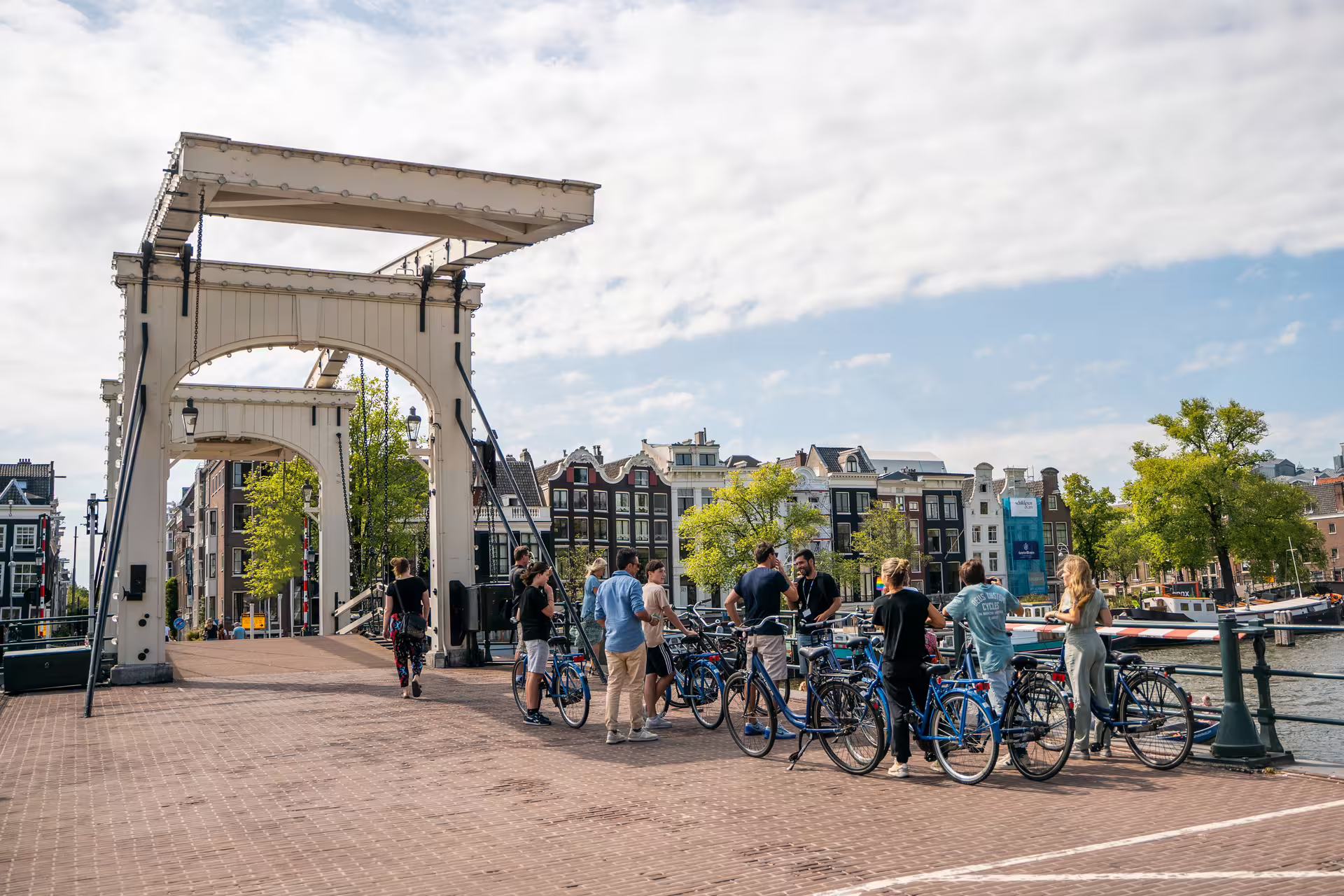Cyclists gather on a picturesque bridge in Amsterdam during a scenic bike tour with canal cruise, cheese tasting, and drinks.