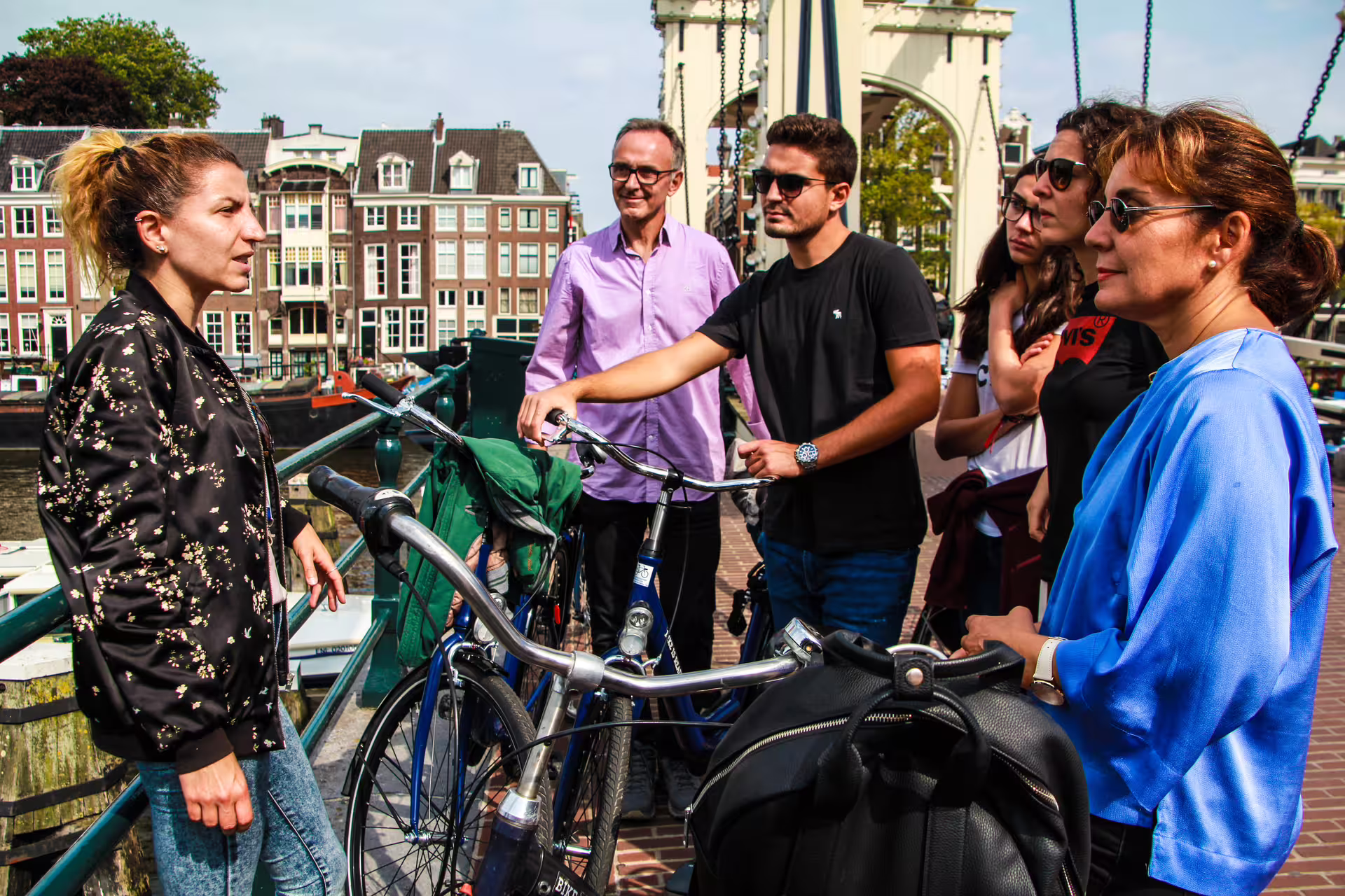 Group of tourists enjoying an Amsterdam bike tour with a guide, featuring scenic views of canal houses and a classic bridge.