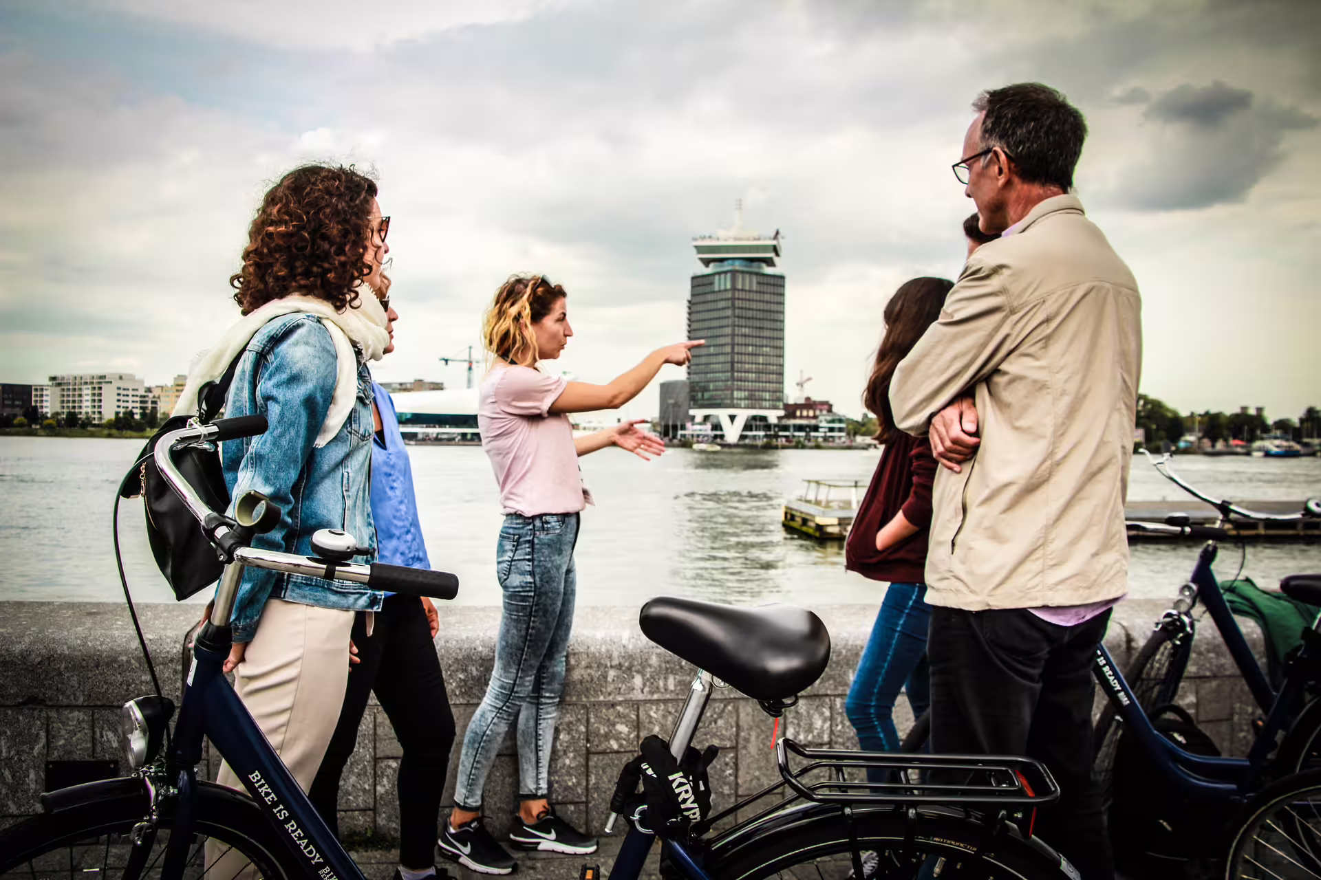 Group of tourists with bikes enjoying a guided tour by Amsterdam's canals, highlighting urban exploration and culture.