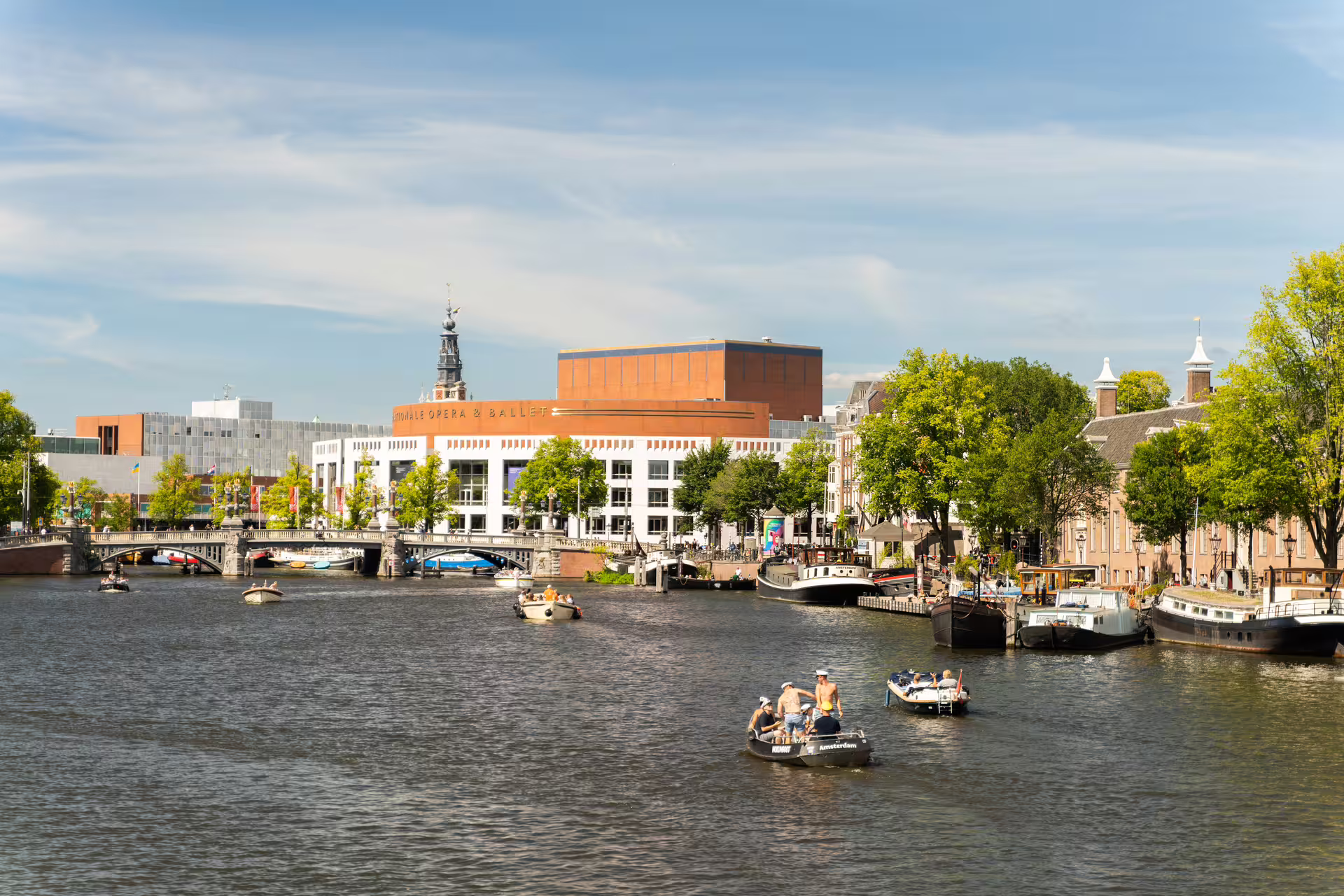 Scenic Amsterdam canal view with boats, lush greenery, and historic architecture, perfect for a bike tour and canal cruise experience.