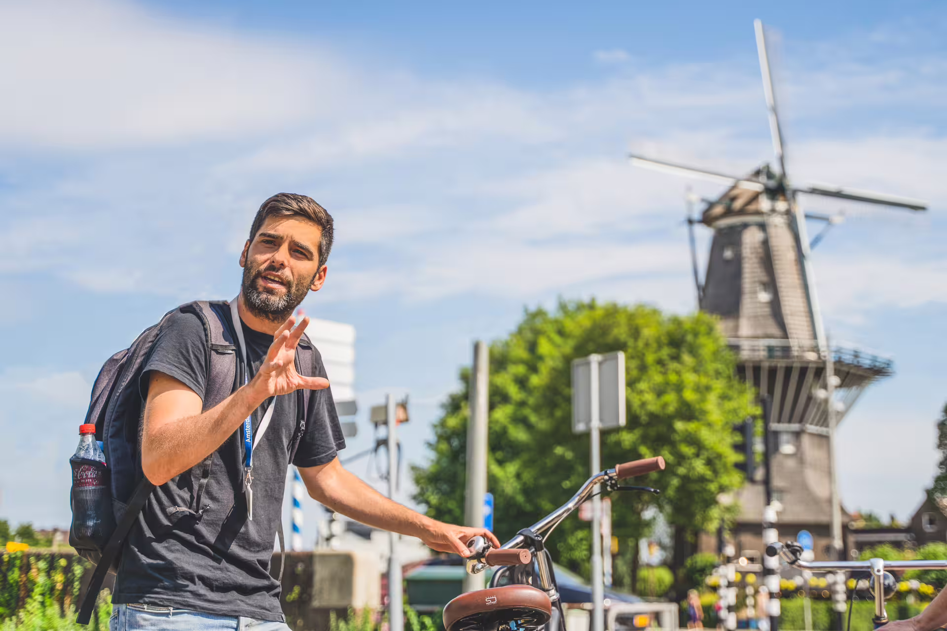 Guide explaining near a bicycle with a scenic countryside windmill backdrop on a private bike tour.