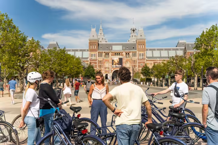 Cyclists gather near the iconic Rijksmuseum in Amsterdam for a scenic bike tour, part of an exciting canal cruise package.