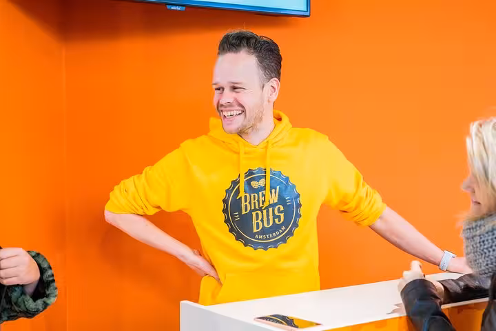 Brew Bus Amsterdam guide in yellow hoodie welcomes guests at check-in for the craft beer brewery tour