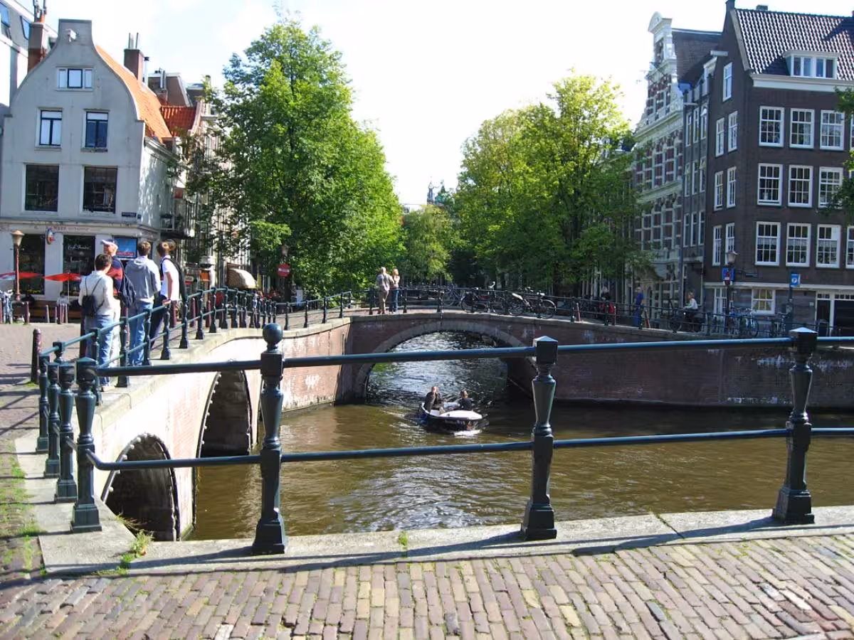 Amsterdam canal bridge with boat and historic buildings, included in private tour from Rotterdam to Kinderdijk and Amsterdam