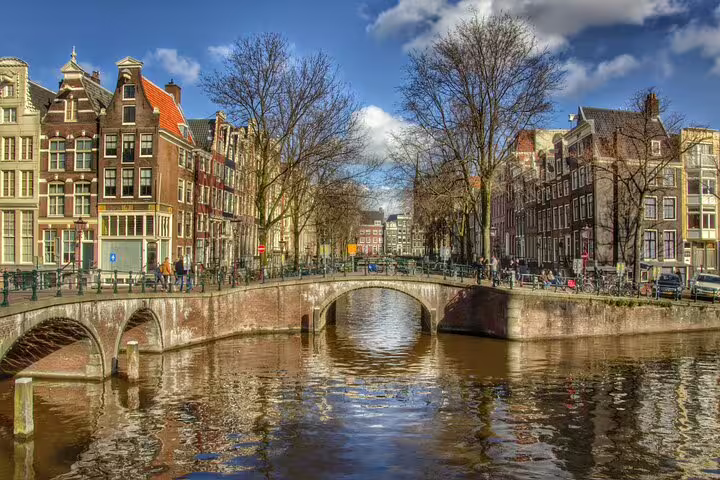 Historic Amsterdam canal bridge with tall Dutch houses, highlight of a 19th century guided private bike tour
