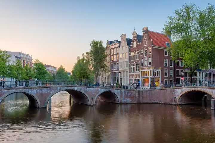 Historic Amsterdam canal bridge at dusk with traditional Dutch gabled buildings reflected in calm water