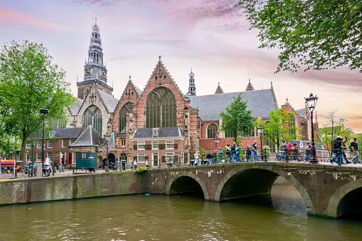 Stone bridge over Amsterdam canal with Oude Kerk gothic church and cyclists in background