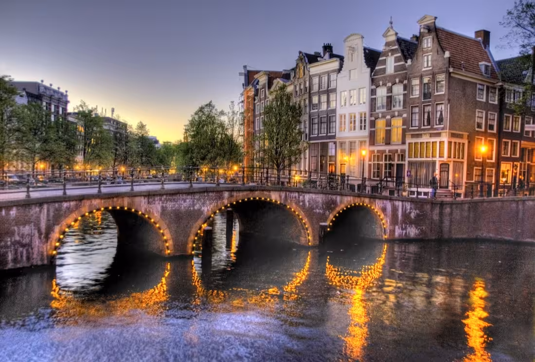 Amsterdam canal bridge at dusk with lit arches and canal houses on private Rotterdam to Kinderdijk and Amsterdam day trip
