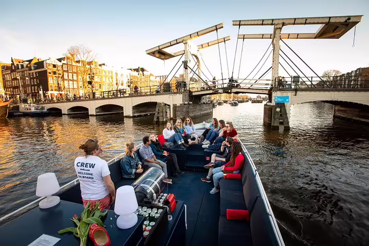 Tourists enjoy a scenic Amsterdam canal cruise with unlimited drinks and cheese tasting, passing under iconic bridges.