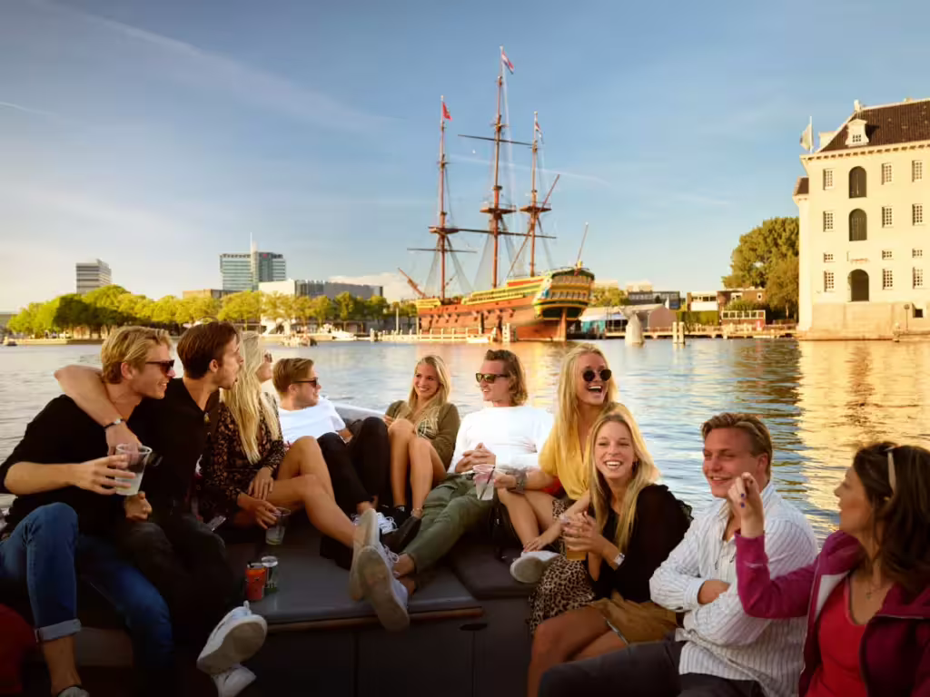 Group enjoying a scenic Amsterdam canal cruise with unlimited drinks, cheese tasting, and historic ship backdrop.