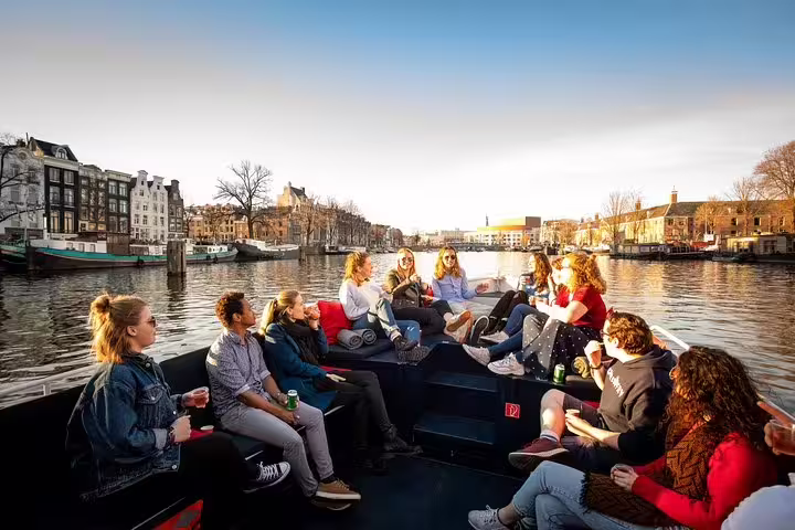 Group enjoying a canal cruise in Amsterdam with unlimited drinks and cheese tasting, showcasing scenic city views.