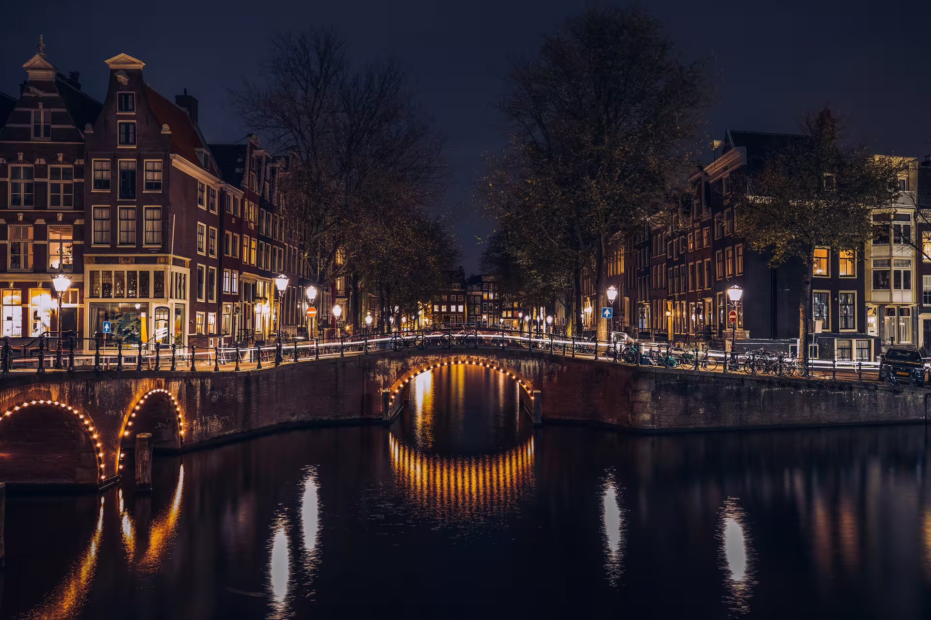 Nighttime Amsterdam canal bridge lights reflecting on water, scenic canal cruise stop on a 4-hour layover tour