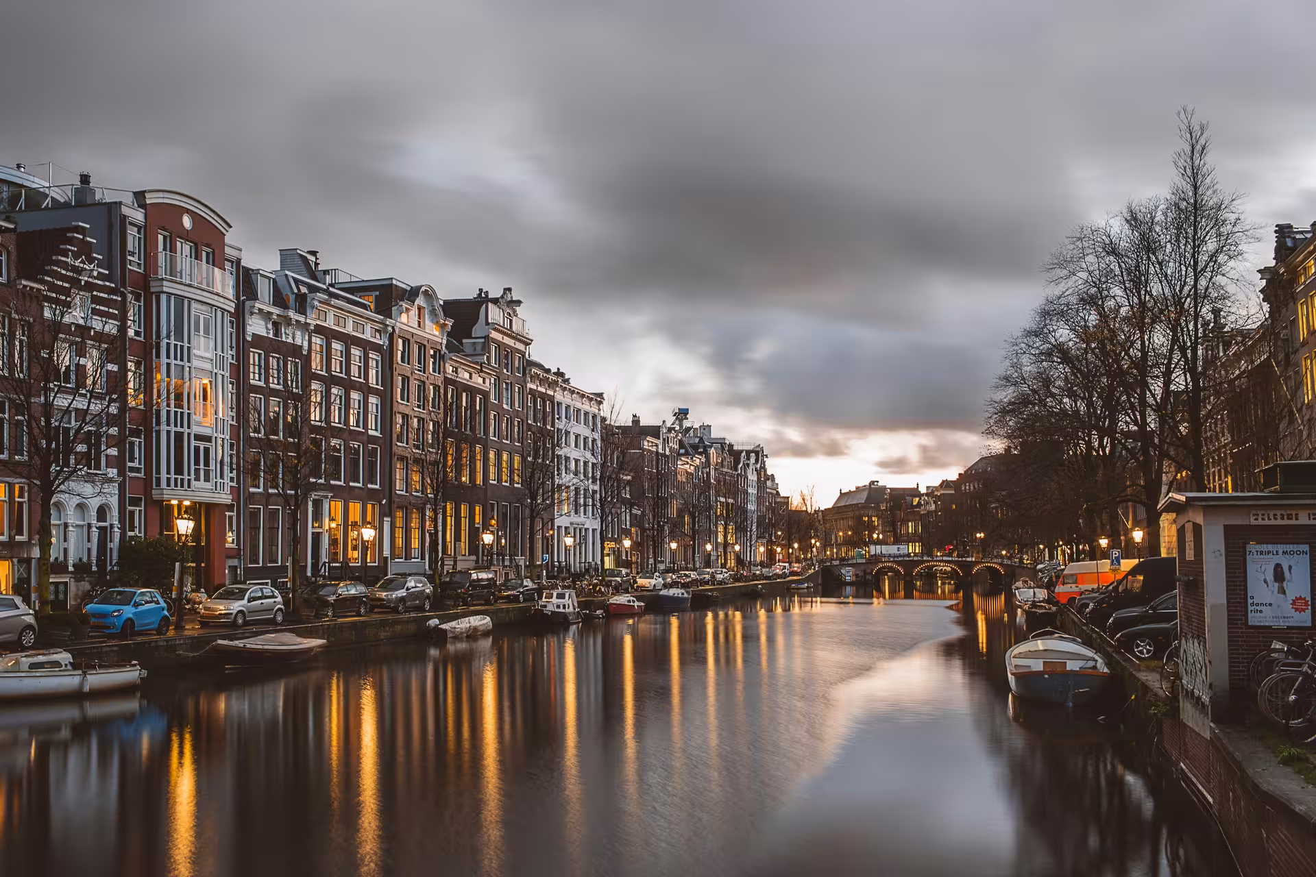 Amsterdam canal at dusk with illuminated bridges and houseboats, ideal stop on a private Schiphol layover tour