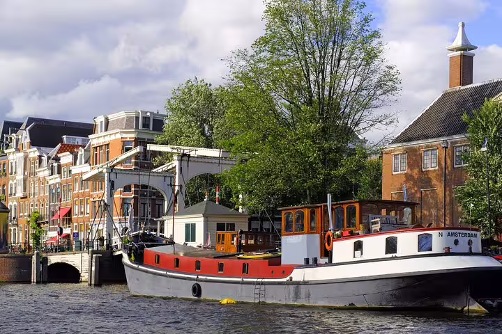 Historic Amsterdam canal with traditional houseboat and bridge on a 19th century private bike tour route