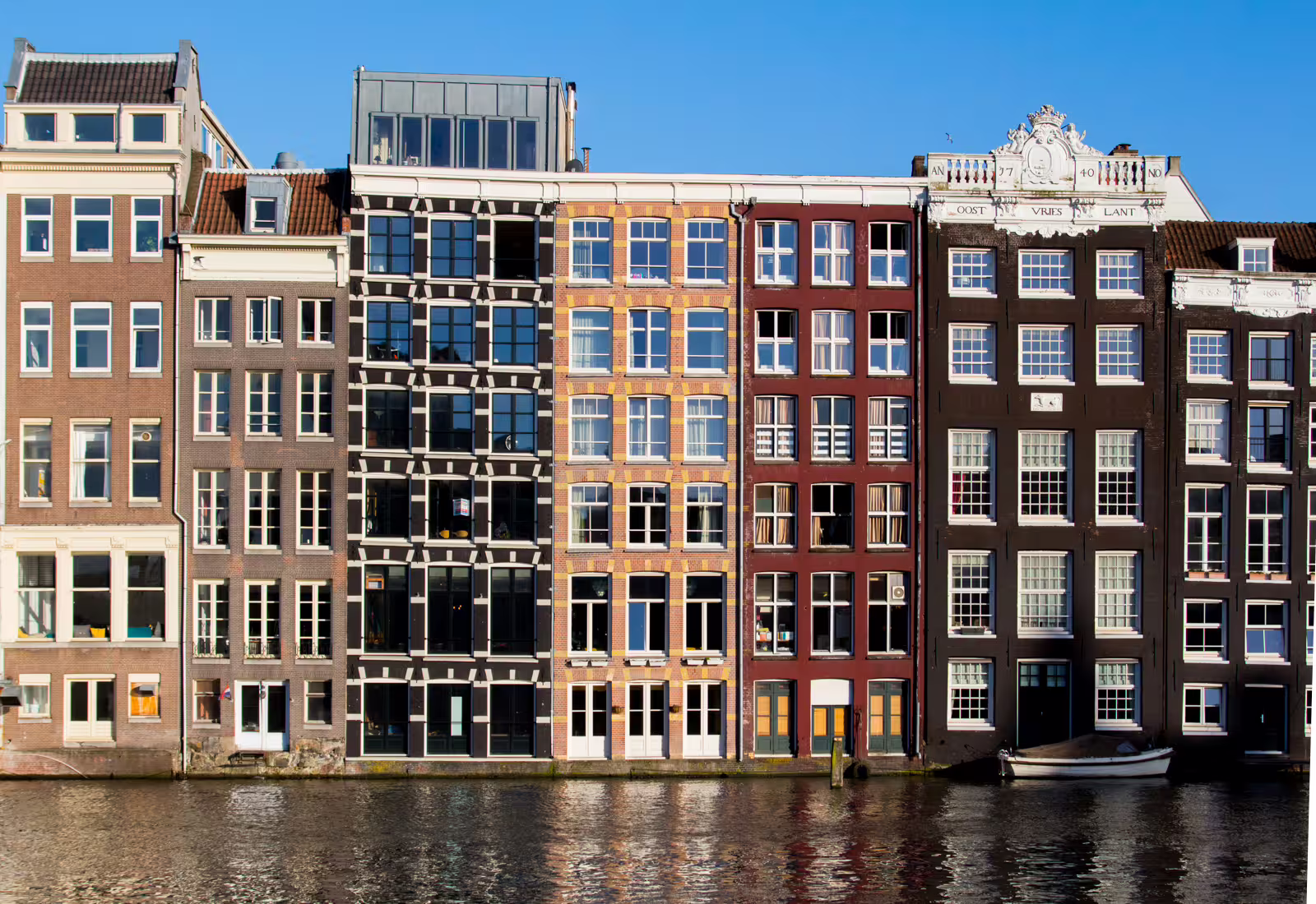 Historic canal houses reflecting in water, showcasing Amsterdam's iconic architecture on a sunny day, ideal for walking tours.
