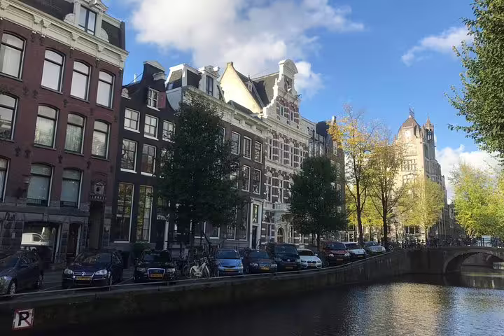 Amsterdam canal houses and tree-lined waterfront, scenic stop on unexpected treasures walking tour