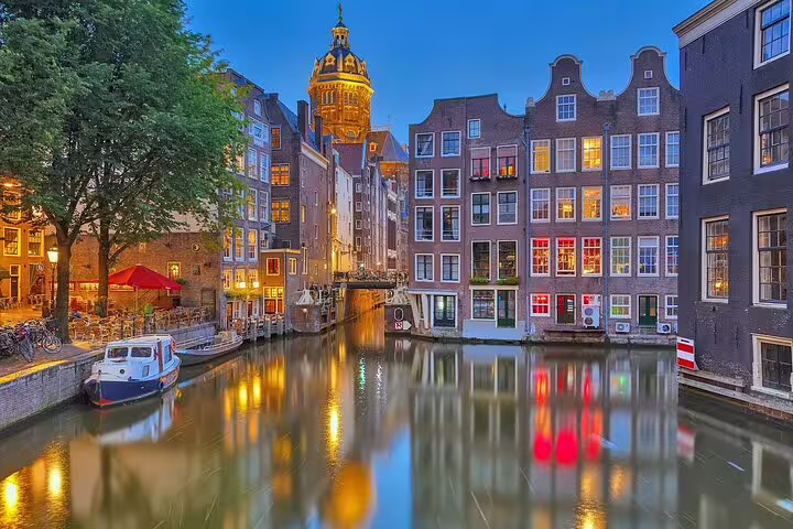 Amsterdam canal at dusk with illuminated historic gabled houses and church tower reflecting in calm water
