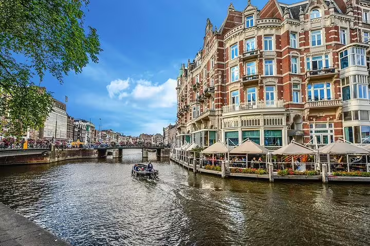 Amsterdam canal view with historic waterfront buildings and boat, private half-day sightseeing tour stop