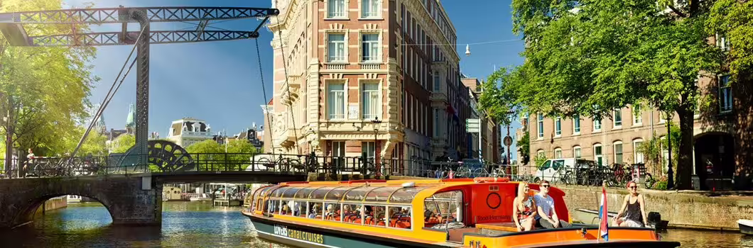 Vibrant canal scene in Amsterdam featuring a tour boat under a historic bridge, perfect for walking, biking, and cruising adventures.