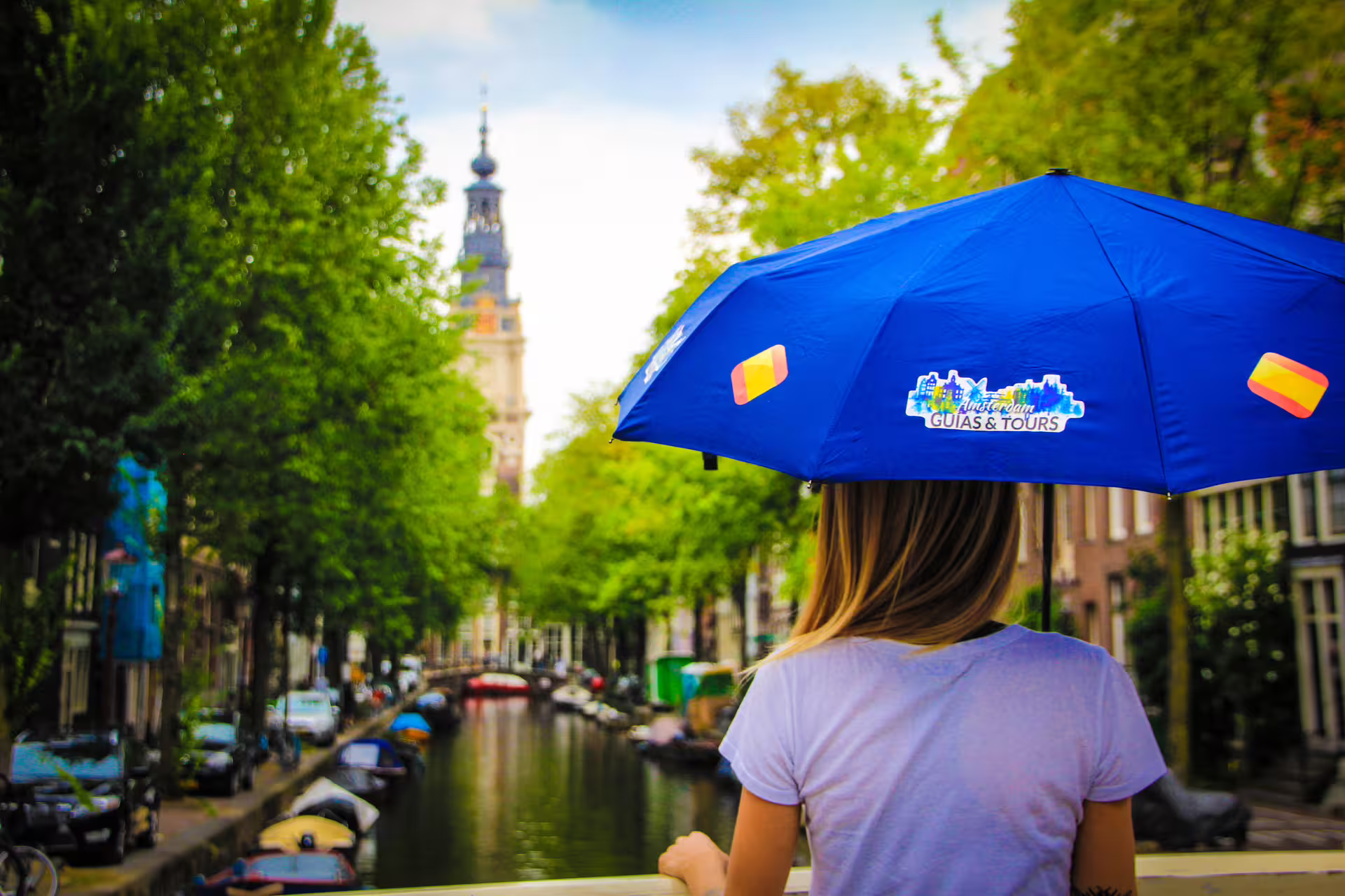 Woman with blue umbrella overlooking Amsterdam canal, highlighting walking, biking, and pancake cruise tour experience.