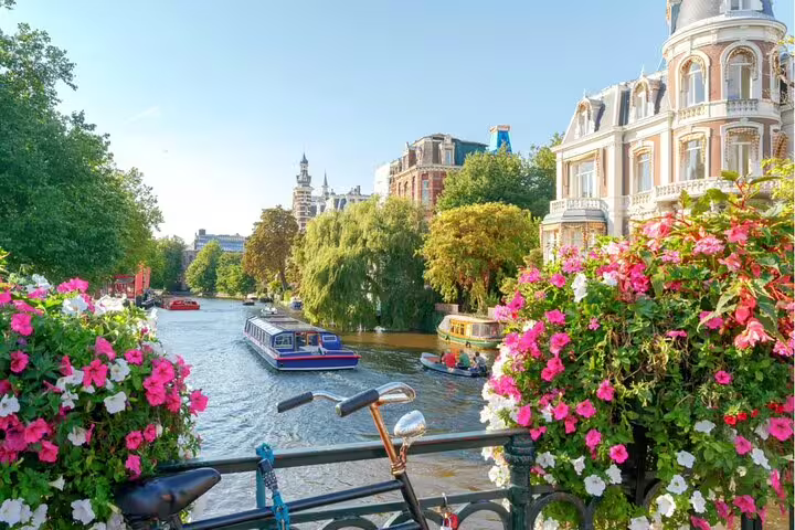 Amsterdam canal with tour boat, historic mansions, and colorful flowers on a sunny day