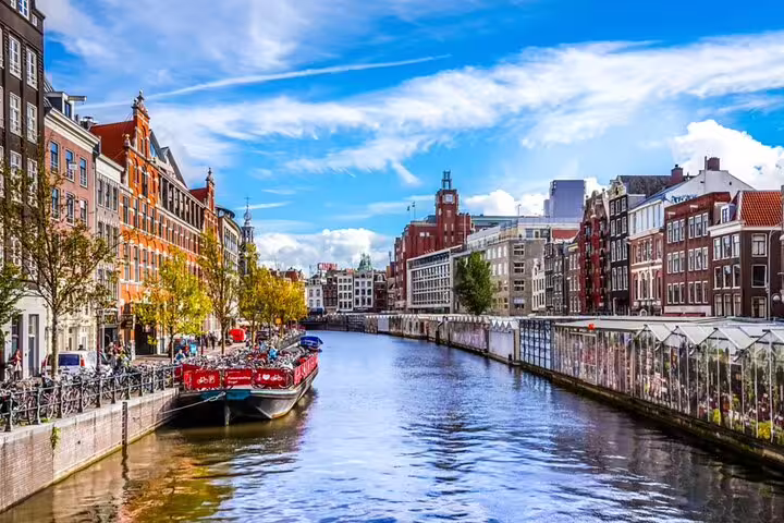 Amsterdam canal with historic brick buildings, moored red boat, bicycles, and blue sky on a sunny day