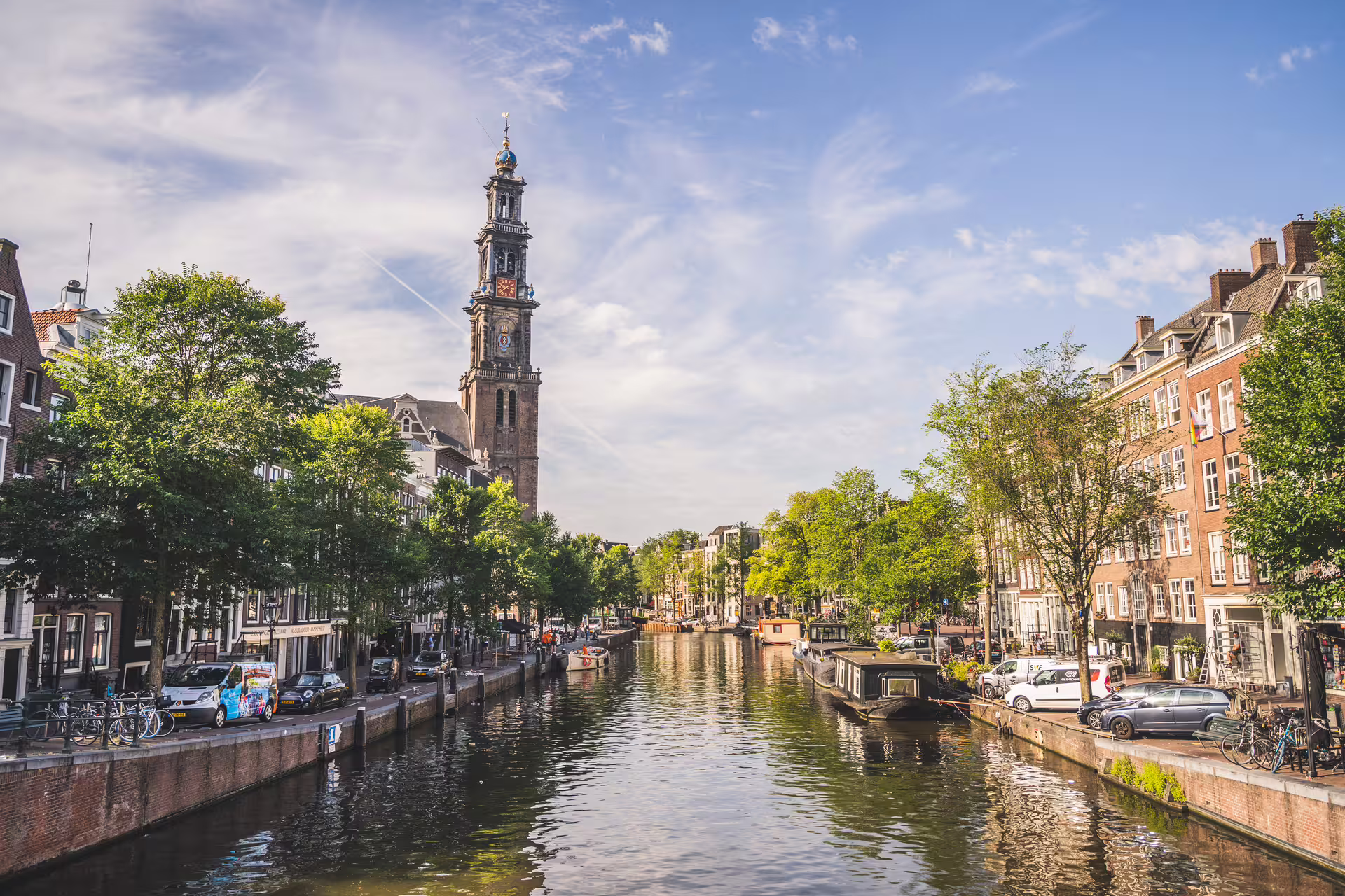 Scenic view of Amsterdam canal with historic architecture and Westerkerk tower, ideal for walking tour and cheese tasting experience.