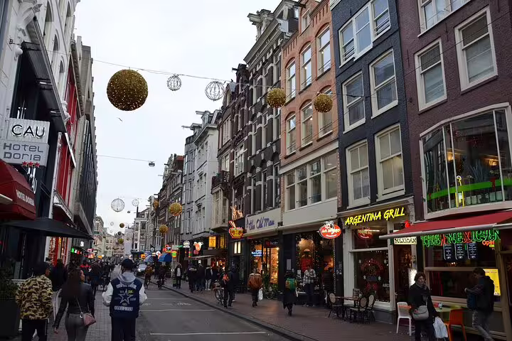 Busy shopping street in Amsterdam with festive golden orb decorations and colorful restaurant signs