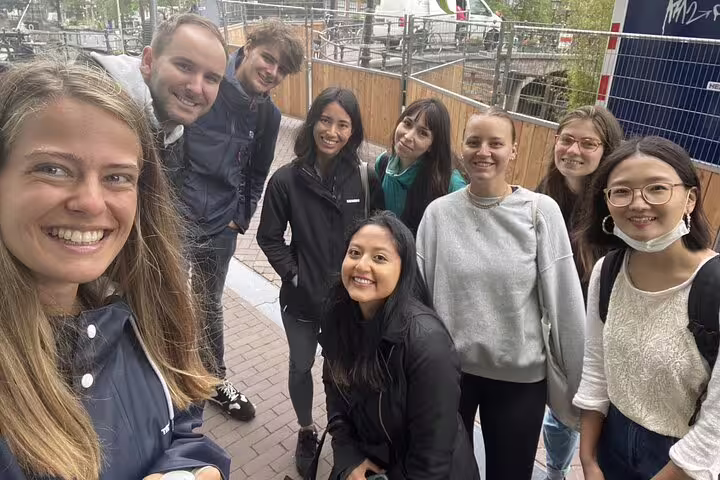 Group of nine smiling friends taking a selfie outdoors in Amsterdam during a city walking tour