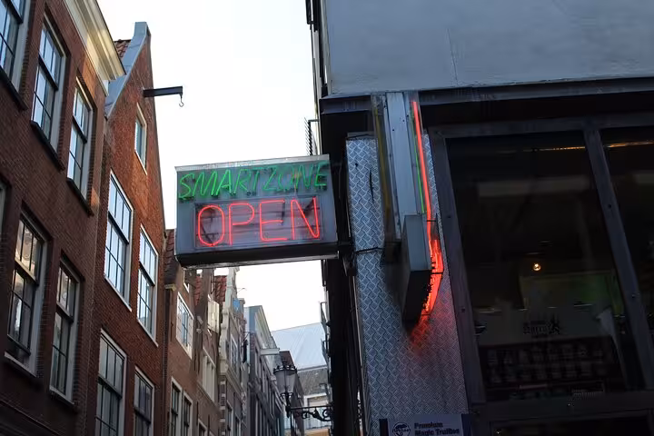 Neon Smart Zone open sign glowing on an Amsterdam coffeeshop street featured in a smartphone app GPS walking tour