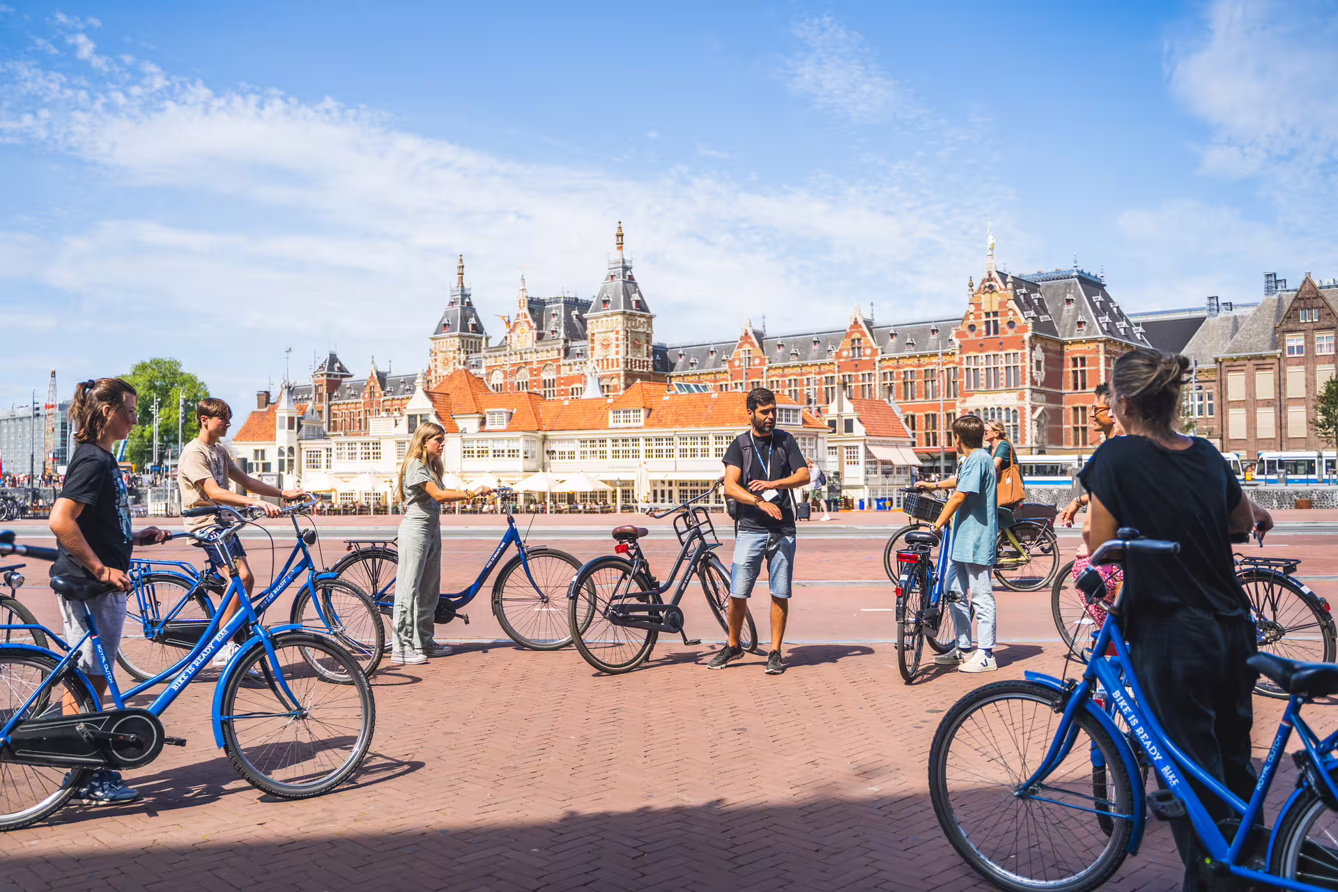Group of tourists on blue bikes exploring Amsterdam's scenic countryside with a historic city backdrop on a sunny day.