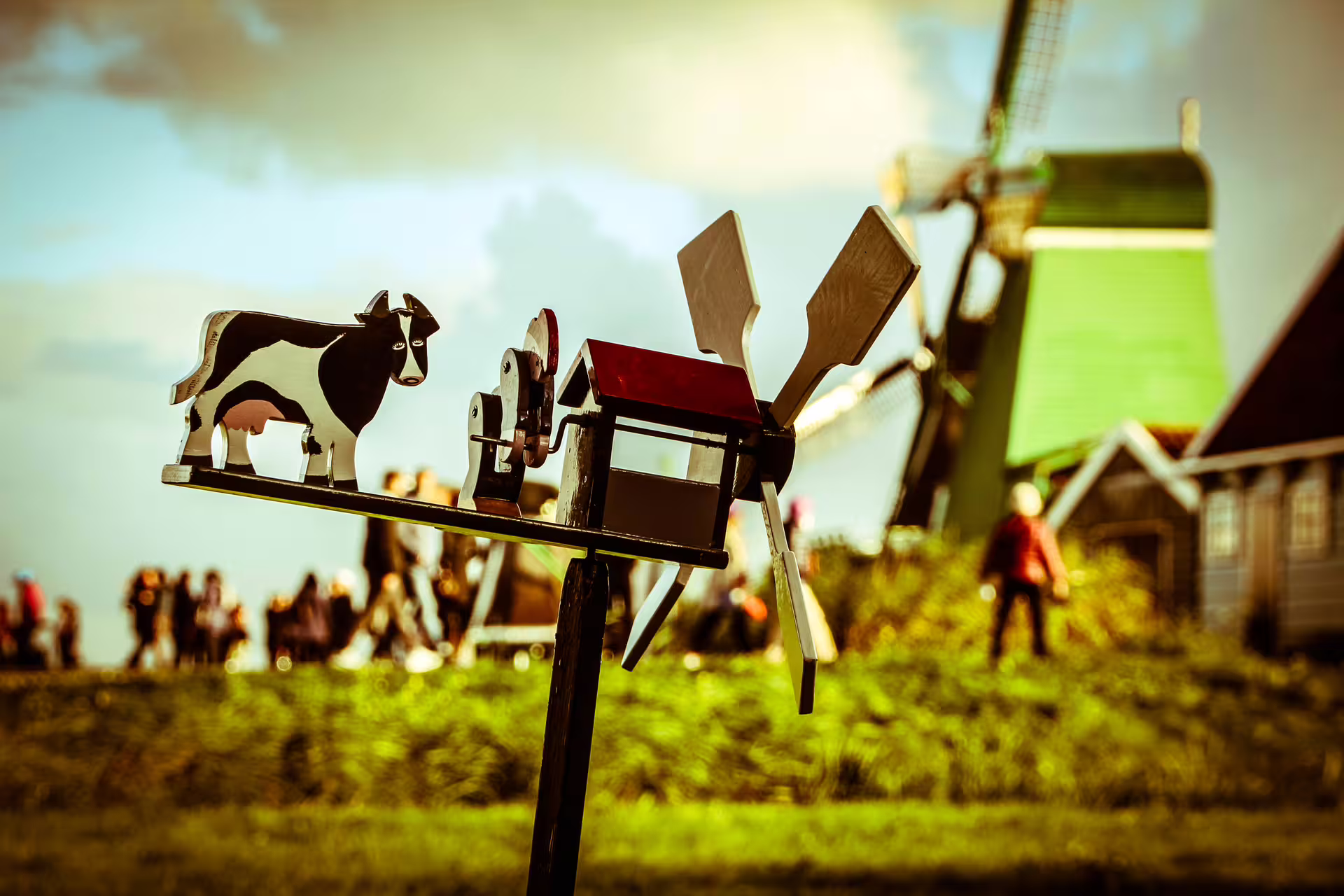 Scenic countryside bike tour with a windmill, wooden cow figurine, and lush greenery under a vast blue sky.