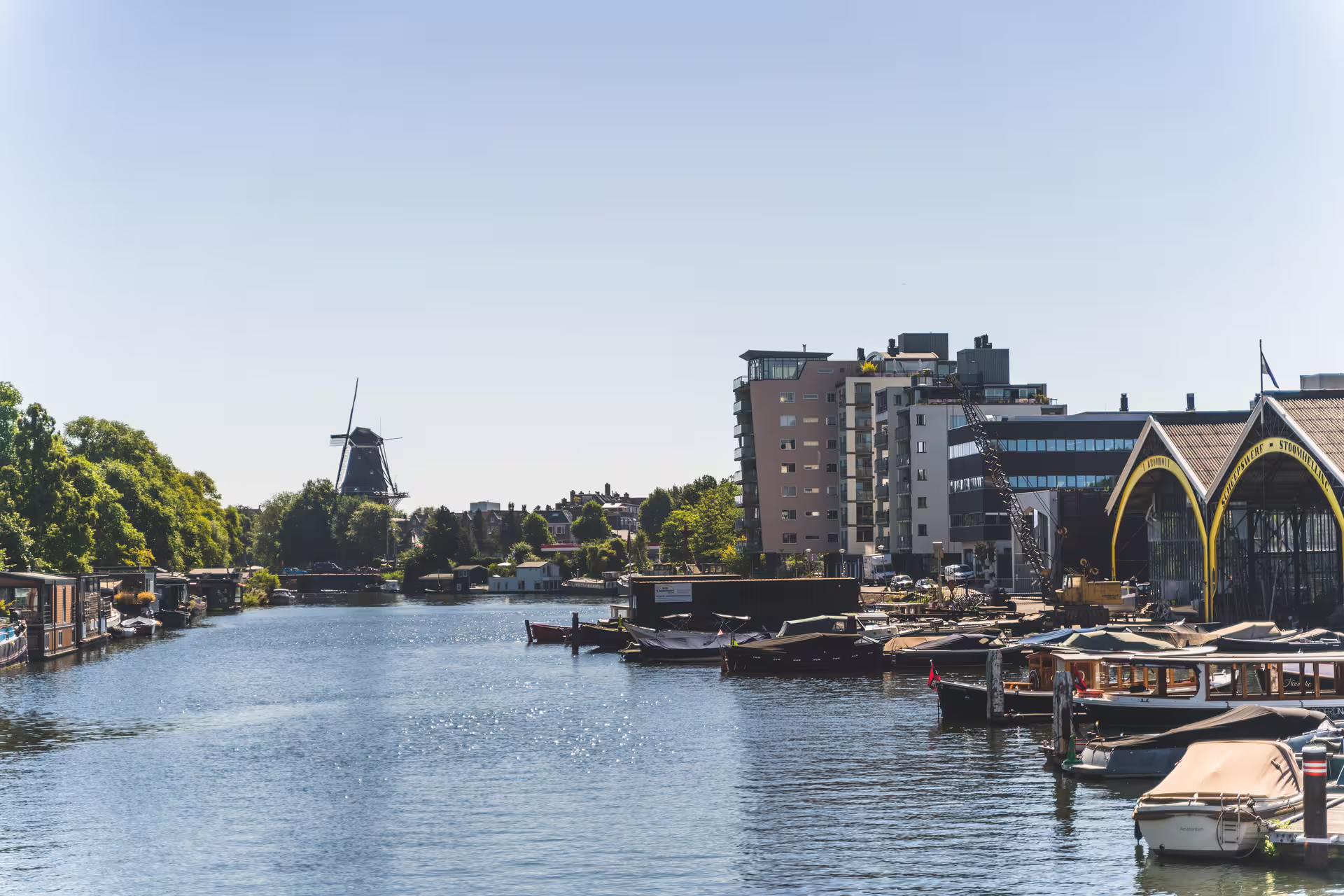 Scenic view of a tranquil canal with boats, surrounded by lush greenery and historic windmill, perfect for a countryside bike tour.