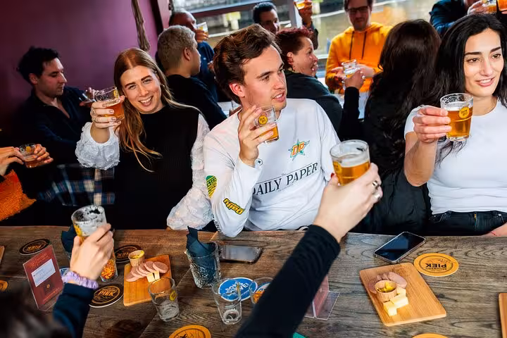 Friends toasting pints on guided Amsterdam craft beer tasting tour with Dutch cheese and sausage board