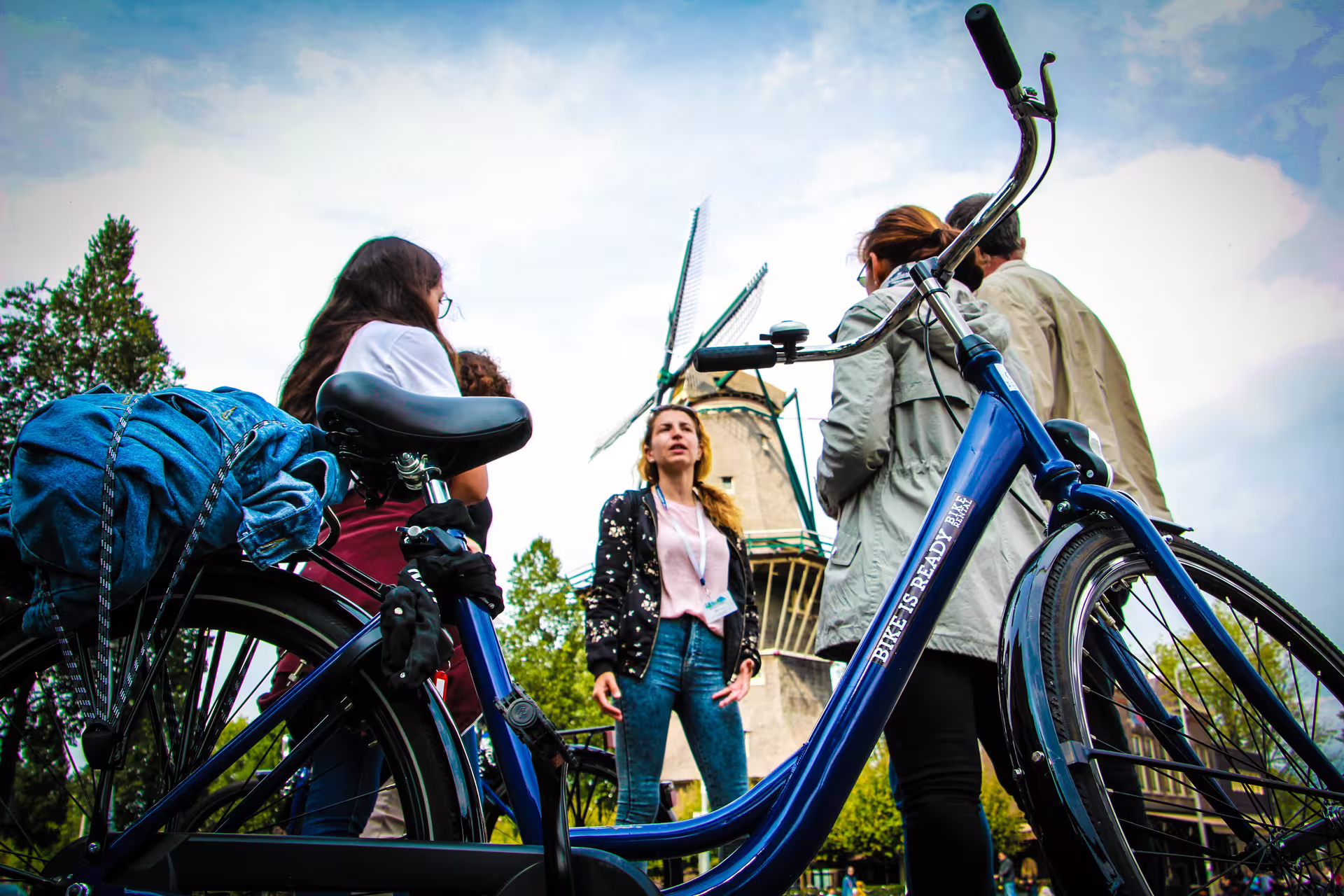 Cyclists gather by a Dutch windmill during an Amsterdam tour, highlighting the city's biking culture and scenic views.