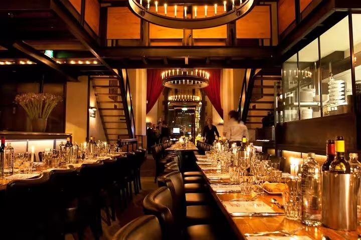 Elegant Amsterdam restaurant interior with candlelit long dining tables, warm lighting, and red curtains
