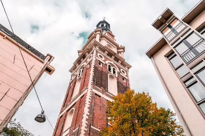 Historic red brick church tower in Amsterdam viewed from below between modern buildings in autumn