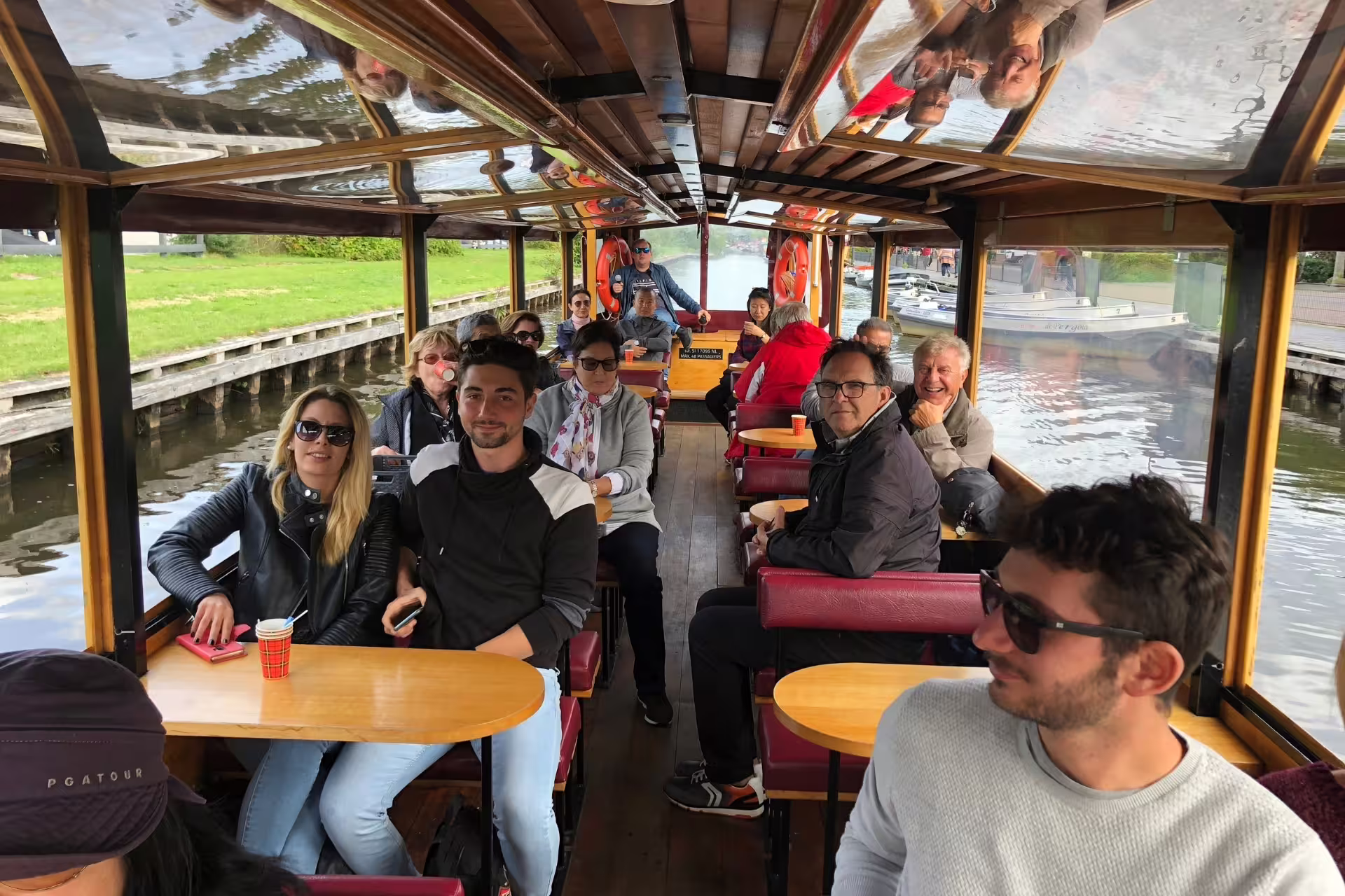Group enjoys a covered canal boat cruise in Giethoorn on an Amsterdam day trip, with tables and scenic waterways