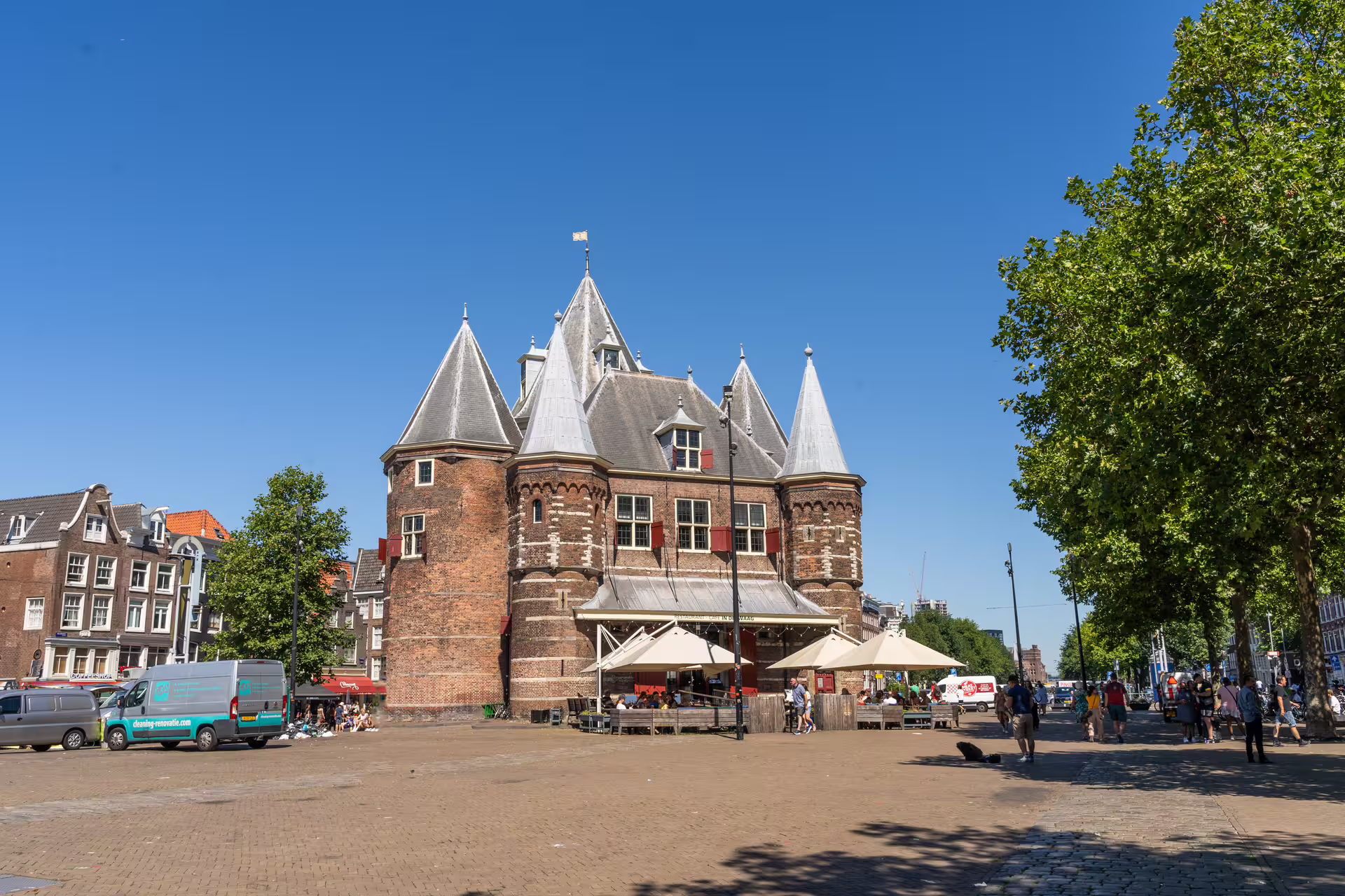 Historic Amsterdam building with turrets under a clear blue sky, bustling with visitors, ideal stop on walking tour with Dutch pancake lunch.