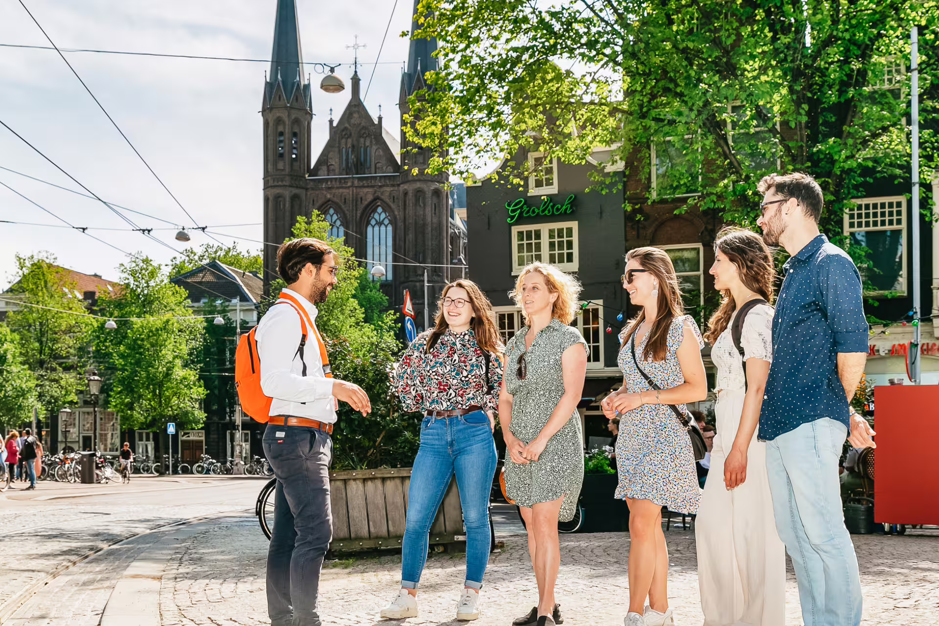 A guide leads a group tour in historical Amsterdam, exploring iconic architecture against a sunny backdrop, perfect for cultural experiences.