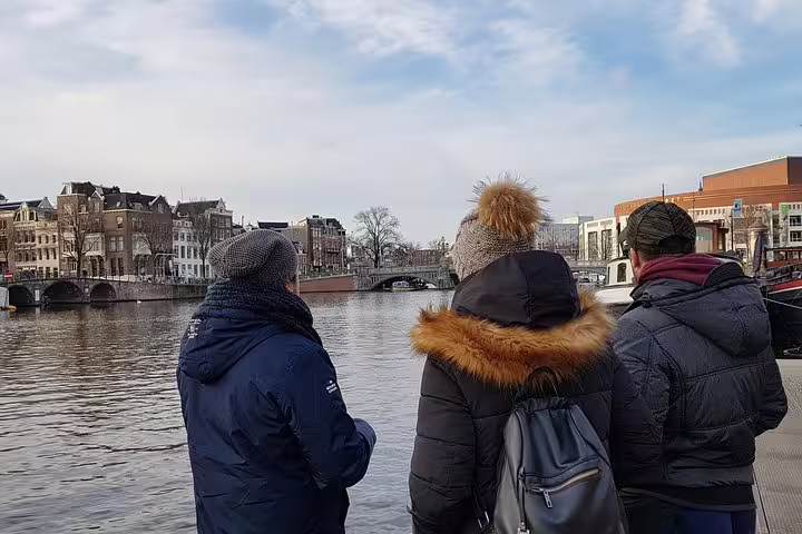 Tourists enjoying a scenic view of Amsterdam's Jewish Quarter along the canal during a private guided tour, winter attire.