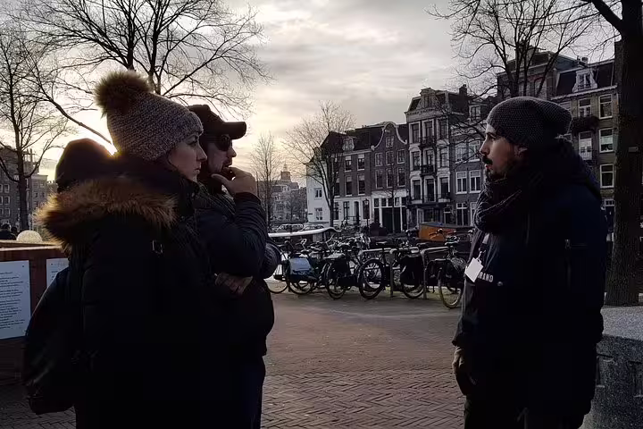 Tourists engage with a guide in Amsterdam's Jewish Quarter, surrounded by historic architecture and bicycles at sunset.