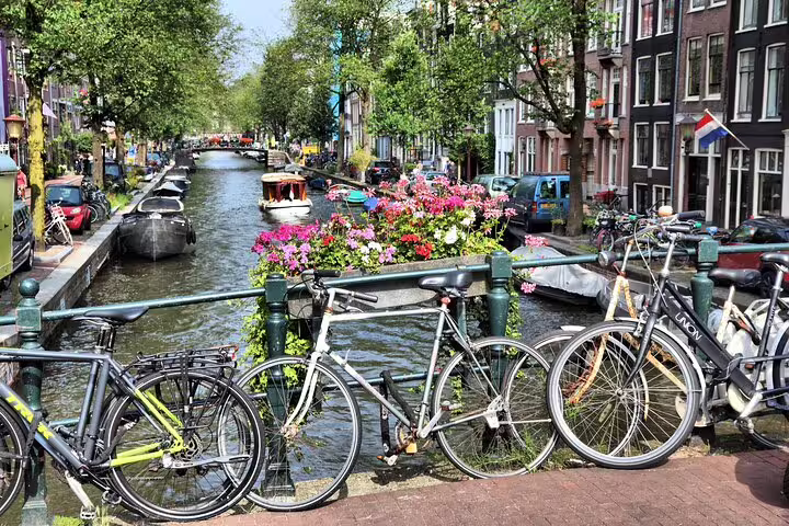 Bicycles leaning on bridge railing over Amsterdam Jordaan canal with colorful flowers and historic buildings