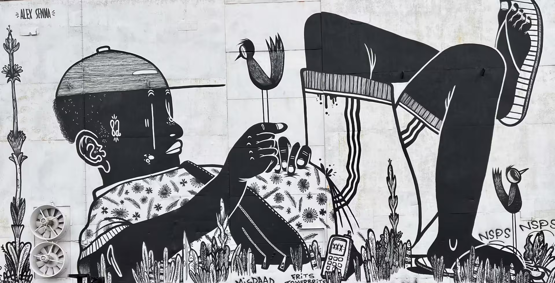 Black and white street art mural at NDSM Amsterdam, featuring a whimsical character holding a bird, symbolizing urban creativity.