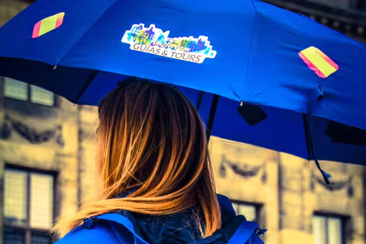 Tour guide in blue jacket with branded umbrella leading an Amsterdam private walking tour in historic city center.